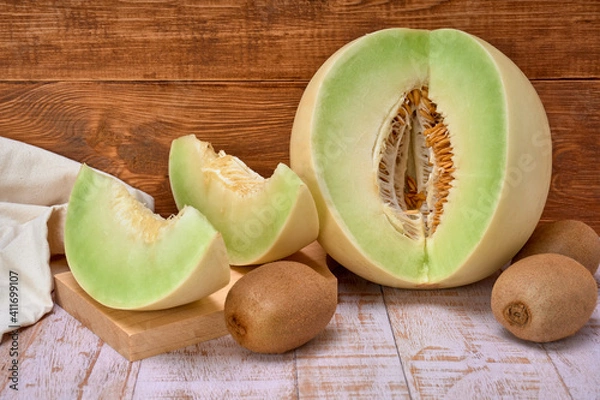 Obraz green melon sliced on wooden board with kiwis and a half melon . over a wooden table and wooden background. healthy food concept. Summer fruit