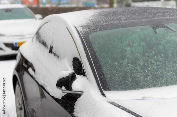 Fototapeta black parked car covered with thick layer of ice and snow in the street in Boskoop, the Netherlands