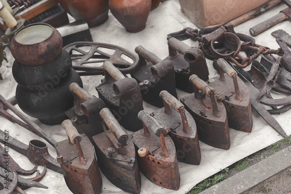 Fototapeta Old rusty original houseware. Outdated charcoal irons, pots and various retro items on sale. Toned