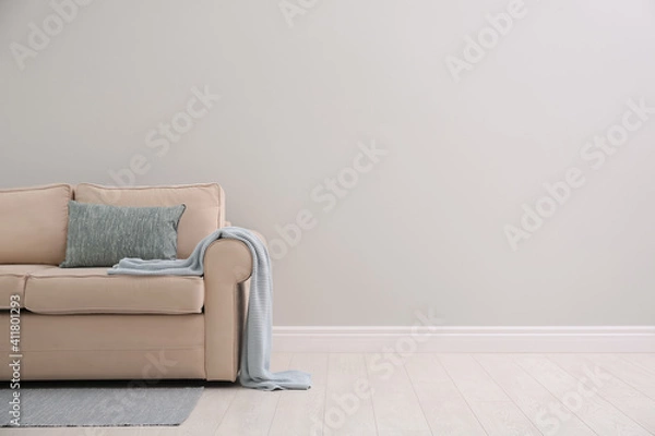 Fototapeta Comfortable beige sofa near light wall indoors, space for text. Simple interior