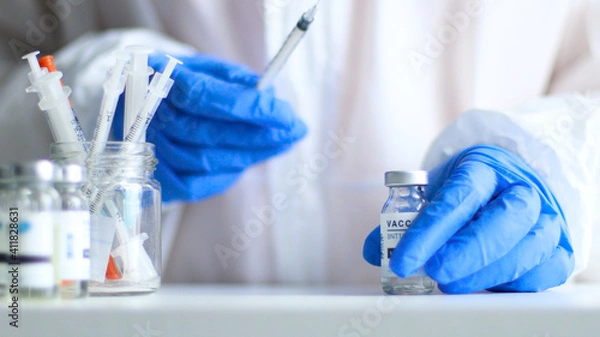 Fototapeta Nurse or doctor in medical protective uniform and latex rubber gloves holding syringe with vaccine while preparing for work during coronavirus, flu or measles pandemic for poster, web banner, article