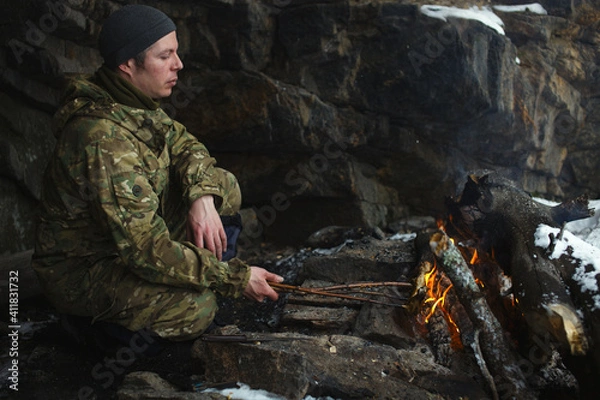 Obraz Traveller roasts a piece of meat on an bonfire near an overhanging cliff, close-up.