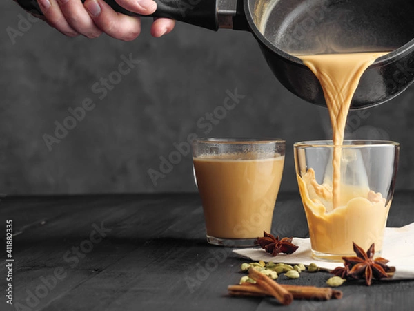 Fototapeta Hot masala tea is poured into a glass glass. Steam comes out of the mug. Gray background. Copy space.