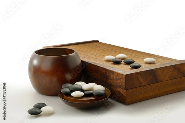 Fototapeta black and white stones of baduk game on wooden board showing white stones surrounding by group of black stones in the corner