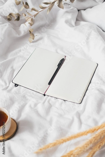 Fototapeta Open notepad with blank pages in textile white background, dried flowers and cup of tea. Tranquil and mindful home living, staying in bed, hand writing in a note book concept