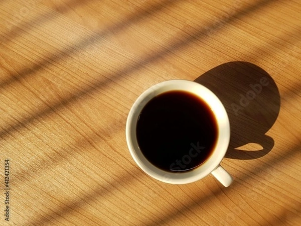 Obraz Top view of cup of coffee on wooden table with warm natural light background and space on the left.