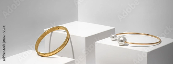 Fototapeta Panoramic shot of Two golden bracelets on white geometric background