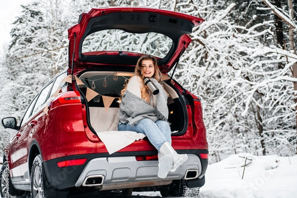 Obraz winter romance concept car travel in winter, in red car drinks hot tea from a thermos, picnic in a frosty winter forest, valentine