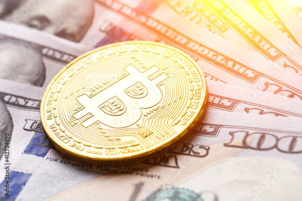 Fototapeta Golden Bitcoin lies on the banknotes.New virtual money. Crypto currency top view. Real coins of bitcoin on banknotes of one hundred dollars. Exchange, commercial. online business concept.