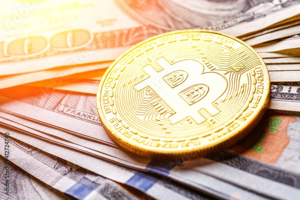 Fototapeta Golden Bitcoin lies on the banknotes.New virtual money. Crypto currency top view. Real coins of bitcoin on banknotes of one hundred dollars. Exchange, commercial. online business concept.