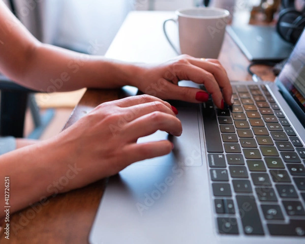Obraz Young brunette woman working and learning from home with a cup of coffee next to her and her notebook