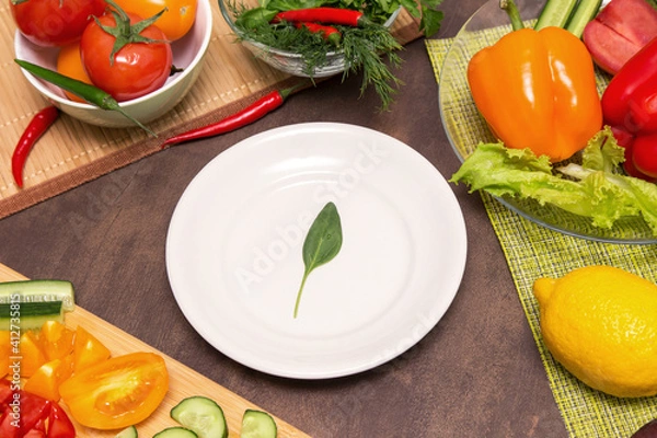 Fototapeta Different vegetables for cooking and one spinach green leaf on white plate. Diet, fasting, vegan, vegetarian, healthy food concept