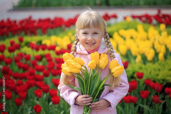 Obraz Portrait of a cheerful little girl on a background of tulips. Girl with a bouquet of yellow tulips. Spring sunny day