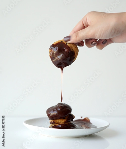 Obraz Woman's hand picking a dark chocolate dipped cookie above cookies stack with melting chocolate in white plate isolated on white background