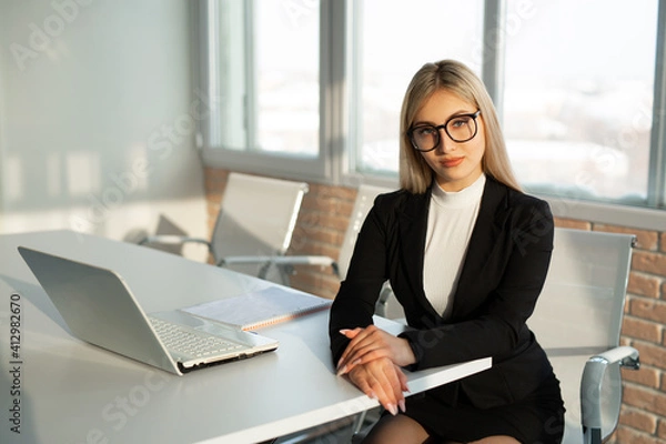 Obraz beautiful young woman in a suit at the office at the table with a laptop 