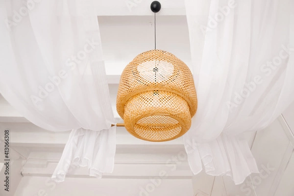 Fototapeta stylish wicker wooden chandelier in boho and Bali style hangs on the ceiling near a white canopy made of weightless tulle. Part of the light airy interior.