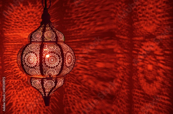 Fototapeta Moroccan lamp with red illuminating patterns of light on textured wall in horizontal position.