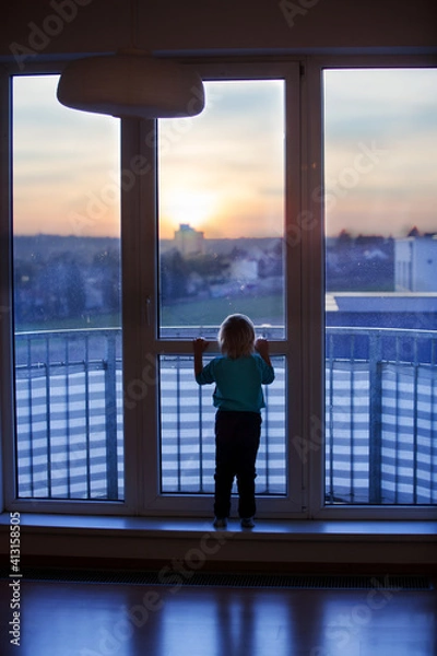 Fototapeta toddler child, sitting on the window on sunset