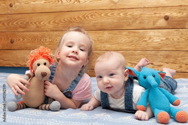 Fototapeta two smiling little children (brother and sister) with toys in denim suits lie on the bed 
