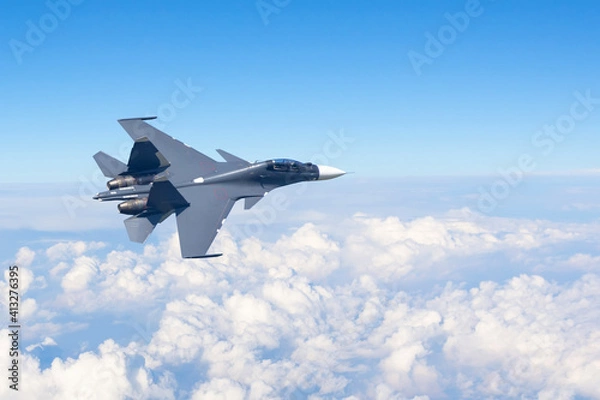 Obraz Combat fighter jet flies turning maneuver high in the sky above the clouds.