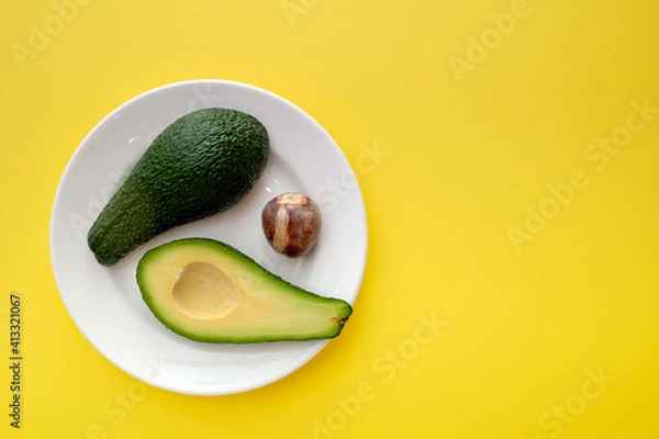 Obraz There are two slices of avocado on the plate. The fruit is divided into two parts. Next to it is an avocado seed. Yellow background color