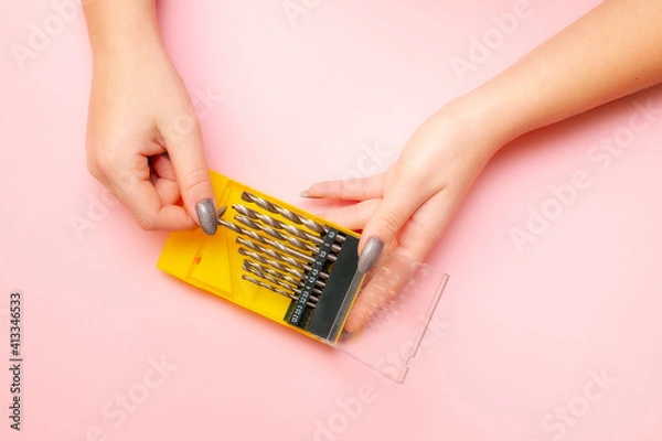 Fototapeta a woman's hand pulls a drill bit out of the box. pink background