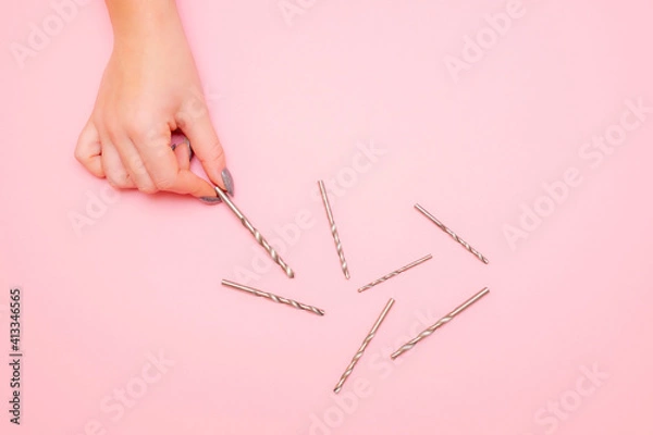 Obraz a woman's hand picks up a drill bit. a pile of drills lies on a pink background
