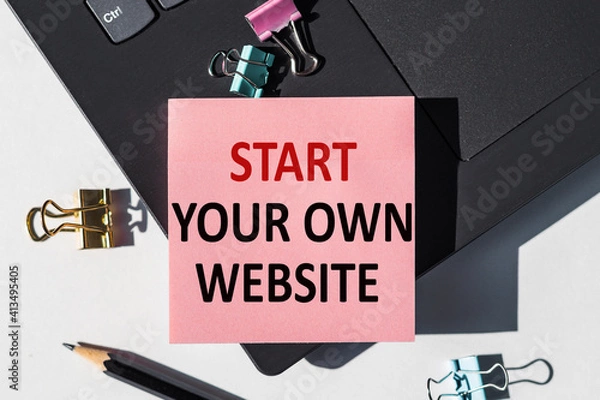 Fototapeta START YOUR OWN WEBSITE note is written on a paper sticker on a laptop keyboard.