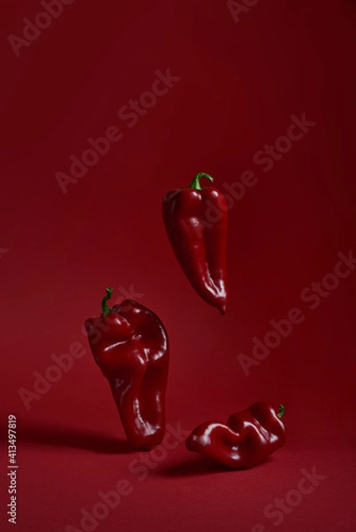 Fototapeta Three red peppers paprika on a red background. Vertical photo
