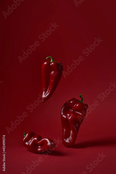 Fototapeta Three red peppers paprika on a red background. Vertical photo