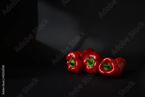 Fototapeta Three whole red sweet bell peppers isolated on black background with light and copy space