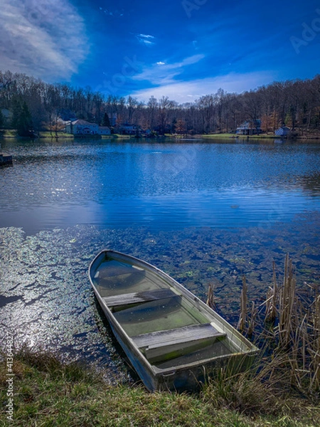 Fototapeta Portrait of a Half-Flooded Boat at the Edge of a Residential Pond on a Bright, Sunny Day with Blue Skies