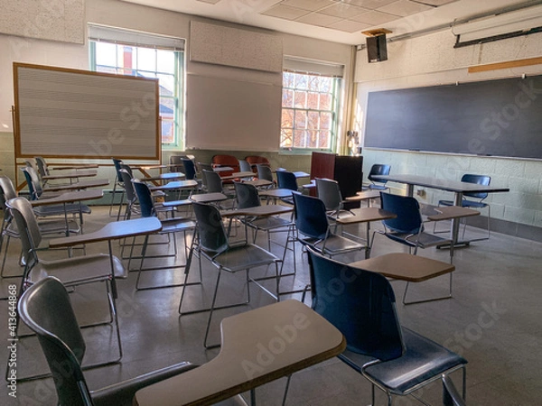 Fototapeta A Shadowy, Empty Classroom in a School with Chairs Facing a Chalkboard on a Sunny Day
