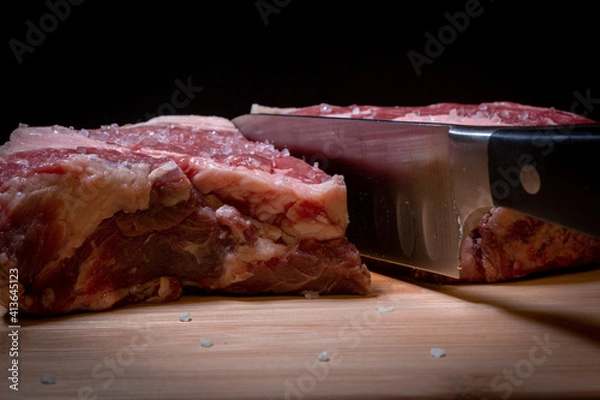 Fototapeta A Knife Cutting through a Raw Piece of Ribeye Steak on a Cutting Board with a Black Background