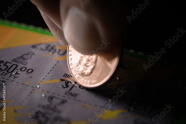Fototapeta Extreme Macro Close-Up of a Caucasian Person's Hand Holding a Penny and Scraping a Scratch-Off Lottery Ticket