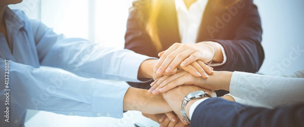 Fototapeta Business team showing unity with their hands together in sunny office. Group of people joining hands and representing concept of friendship, teamwork and partnership