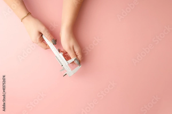 Obraz women's hands hold a caliper. the girl measures the length of her nails. pink background
