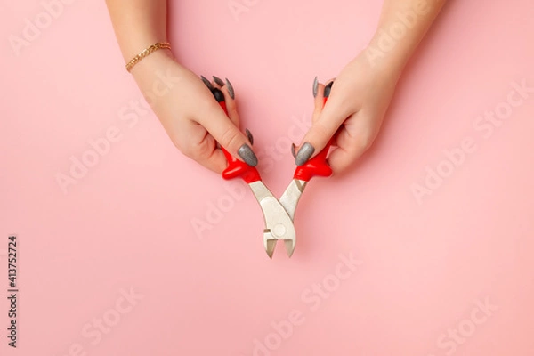 Obraz women's hands hold wire cutters. Wire cutters with electric protection in red on a pink background