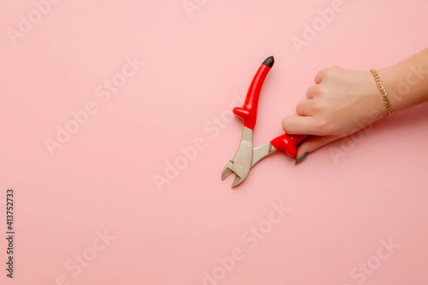 Obraz a woman's hand holds a pair of wire cutters. Wire cutters with electric protection in red on a pink background