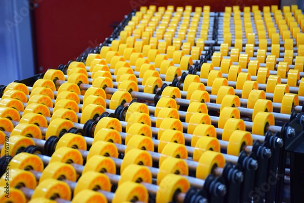 Fototapeta Flexible roller conveyor with variable geometry. transportation of box cargo, ribbon view close up. Yellow roller conveyor belt assembly background. delivery concept