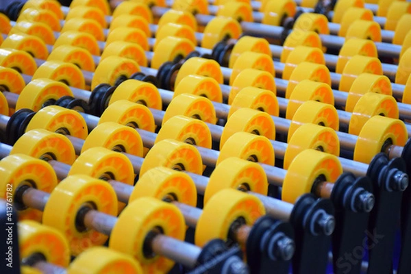 Fototapeta Flexible roller conveyor with variable geometry. transportation of box cargo, ribbon view close up. Yellow roller conveyor belt. delivery concept