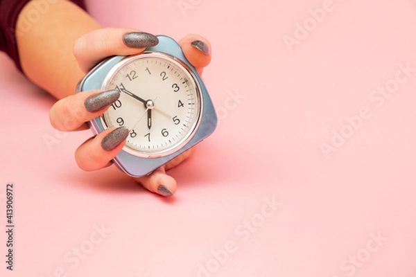 Obraz female hand holds alarm clock on pink background