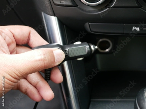 Obraz hand holding plug 12 volt into socket from car cigarette lighter.