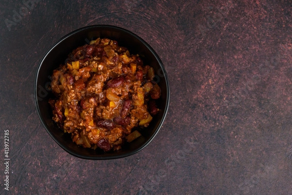 Fototapeta Black bowl of spicy chili con carne on a rustic moody background
