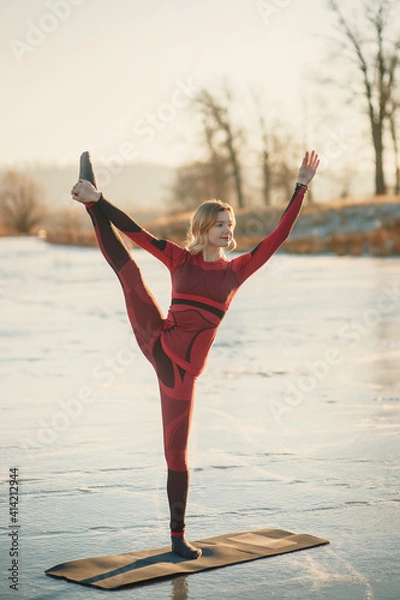 Fototapeta A girl does yoga in winter on the ice of the lake during the sunset