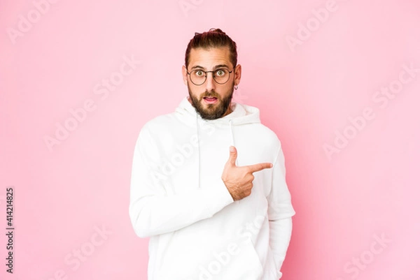 Fototapeta Young man with long hair look smiling and pointing aside, showing something at blank space.