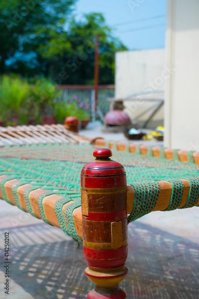 Fototapeta Bokeh style photo of charpai desi Indian Pakistani traditional bed made of woven rope mesh with beautiful red legs.