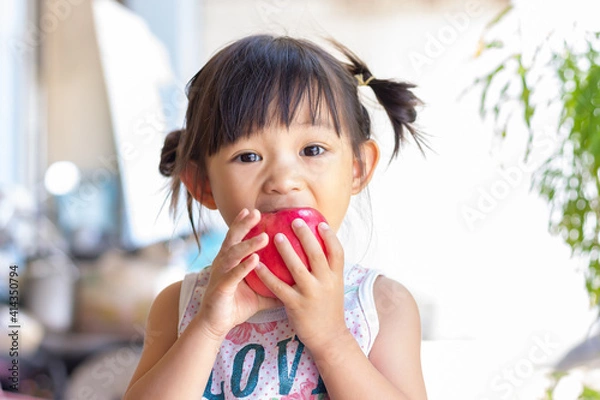 Fototapeta Portrait​ image​ of​ 2-3 yeas​ old​ of​ baby.​ Happy​ Asian child girl eating and biting an red apple. Enjoy eating moment. Healthy food and kid concept.​