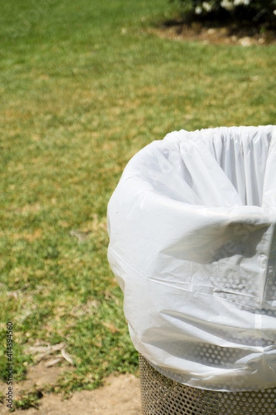 Fototapeta Trash bin in a park with white plastic bag