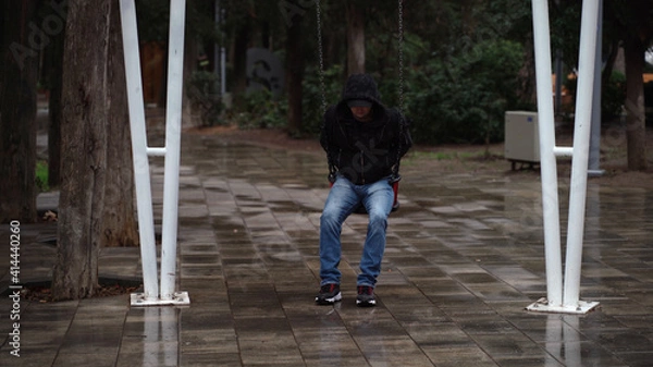 Fototapeta Lonely man in the park swinging on a swing. A sad man in depression is lonely swinging on a swing in an empty winter park.